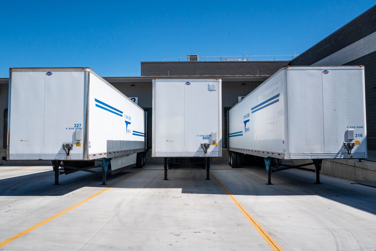 Three white cargo trailers parked at an industrial shipping dock under clear blue skies.